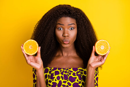 Portrait of charming dark skin lady kiss lips hands hold half orange look camera isolated on yellow...