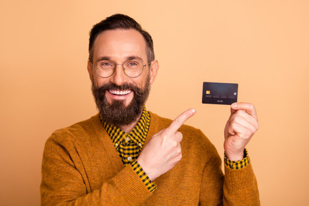 Photo of optimistic brown hair man point card wear spectacles brown sweater isolated on beige color backgroundの写真素材