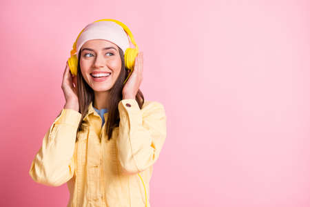 Photo of delighted cute lady arms touch earphones look empty space isolated on pastel pink color...