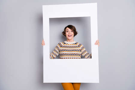 Portrait of lovely funny cheerful girl holding in hands big photo frame isolated over grey pastel color backgroundの写真素材