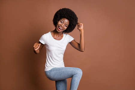 Photo of cheerful winner lady raise fists open mouth wear white t-shirt jeans isolated brown color backgroundの写真素材