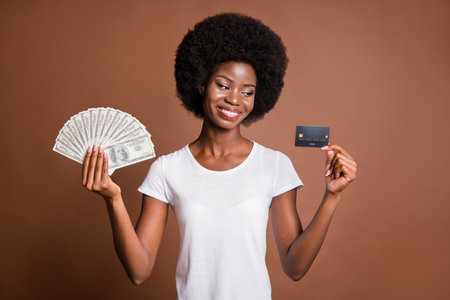 Photo portrait of woman looking at credit card keeping banknotes dollars salary isolated on brown color backgroundの写真素材