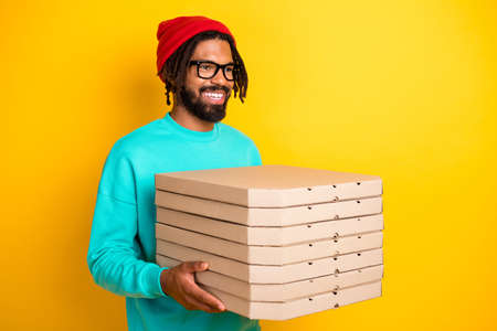 Profile portrait of brunette optimistic guy hold pizza wear cap spectacles blue pullover isolated on yellow vivid color backgroundの写真素材