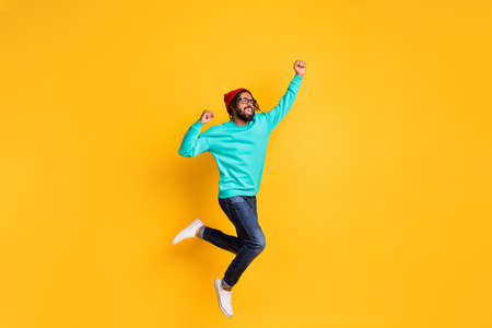 Full size profile photo of brunette optimistic guy jump wear cap spectacles pullover jeans sneakers isolated on yellow color backgroundの写真素材