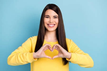 Portrait of nice optimistic brunette long hairdo lady show heart wear yellow shirt isolated on bright blue color backgroundの写真素材