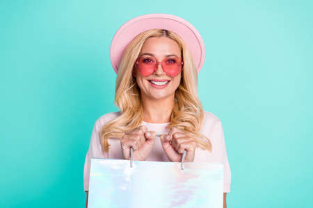 Portrait of charming cheerful wavy-haired woman holding in hands bag new things isolated over bright teal turquoise green color backgroundの写真素材