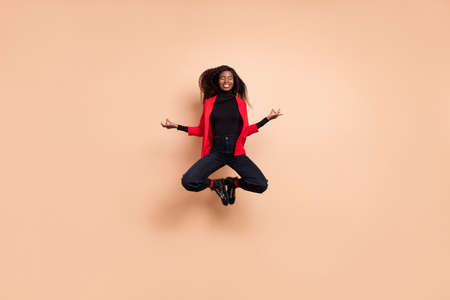 Photo of cute concentrated curly dark skin woman dressed red blazer jumping open chakras isolated beige color backgroundの写真素材