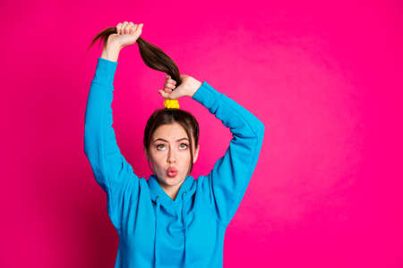 Portrait of pretty young girl kiss lips look up hands hold hairstyle tail isolated on pink color backgroundの写真素材