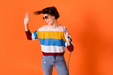 Photo of attractive carefree person arm hold mic look empty space palm wave isolated on orange color...