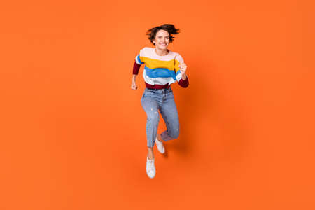 Photo of pretty cute young woman wear striped sweater jumping running fast isolated orange color...