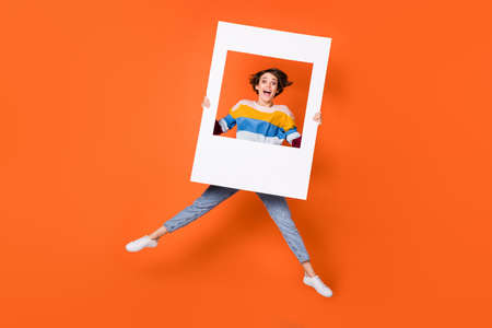Full size photo of astonished girl jumping hands hold frame open mouth isolated on orange color...