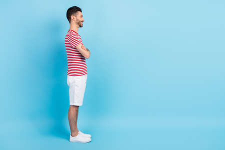 Full length profile side photo of charming man look empty space hold hands crossed isolated on blue...