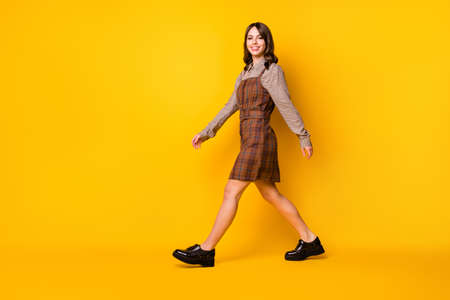 Full size profile photo of optimistic brunette lady go wear brown shirt dress boots isolated on vivid yellow color backgroundの写真素材