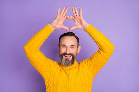 Photo of romantic bearded man raise hands show heart figure wear yellow pullover isolated violet...
