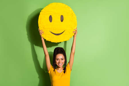 Portrait of nice cheerful girl rising up holding in hands large yellow smile face isolated over bright green color backgroundの写真素材