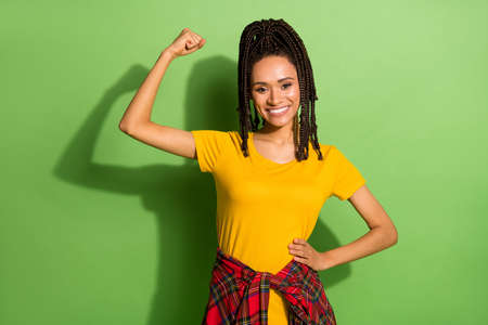 Photo of sweet sporty dark skin lady dressed yellow t-shirt rising fists showing muscles isolated green color backgroundの写真素材