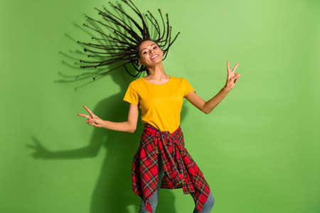 Portrait of pretty carefree cheerful girl throwing braids showing v-sign having fun isolated over bright green color backgroundの写真素材