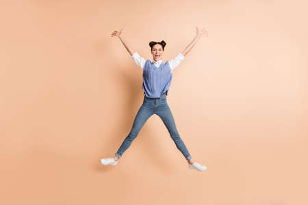 Full size photo of brunette optimistic lady jump wear white shirt blue vest jeans sneakers isolated on beige color backgroundの写真素材