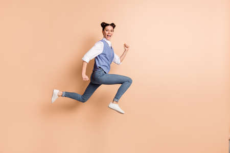 Full length photo of cute adorable young lady wear blue vest jumping high running fast isolated beige color backgroundの写真素材