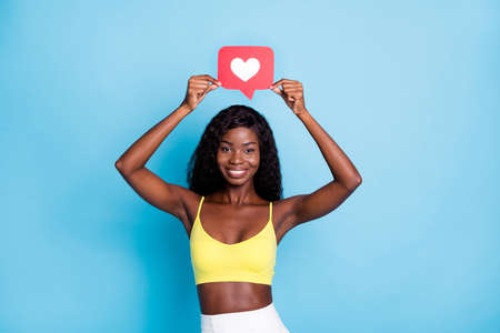 Photo of cute pretty dark skin curly girl dressed yellow singlet holding red like card isolated blue color backgroundの写真素材