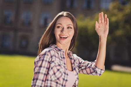 Photo of young cheerful girl student happy positive smile look empty space wave hand hello outside parkの写真素材