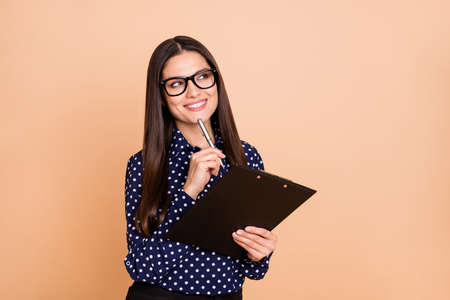 Portrait of attractive lady pen touch chin look empty space thinking dream toothy smile isolated on beige color backgroundの写真素材