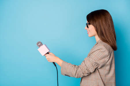 Photo portrait side profile of woman holding microphone with blank space isolated on vivid blue colored backgroundの写真素材