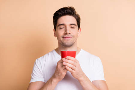 Photo of satisfied person arms hold coffee cup closed eyes nice smelling isolated on beige color backgroundの写真素材