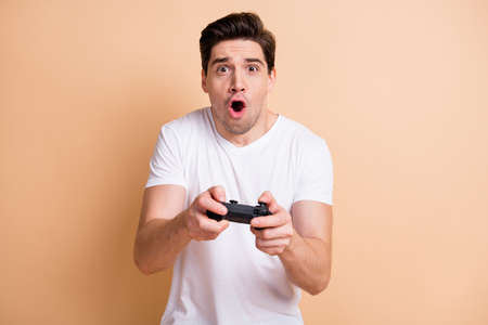Photo of impressed young guy gamer open mouth yelling excited game isolated on beige color backgroundの写真素材