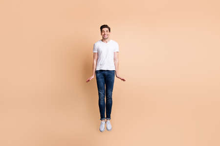 Full size photo of optimistic brunet man jump wear t-shirt jeans sneakers isolated on beige backgroundの写真素材