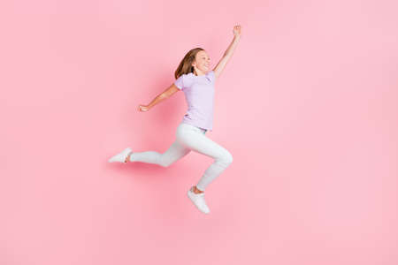 Full size profile side photo of blonde small girl jump up raise fist look empty space isolated on pink color backgroundの写真素材
