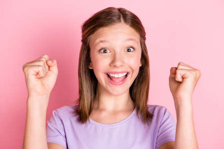 Photo of cheerful happy charming small girl raise fists winner good mood isolated on pink color backgroundの写真素材