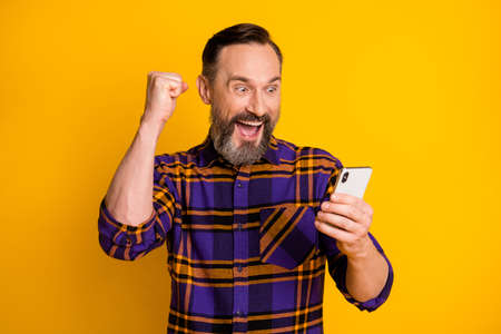 Photo portrait of happy smiling man with smartphone gesturing like winner happy isolated on vibrant yellow color backgroundの写真素材