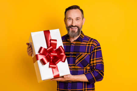 Portrait of attractive cheerful guy wearing checked shirt holding in hands bow ribbon box isolated over bright yellow color backgroundの写真素材