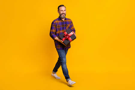 Full length photo of charming attractive man go empty space hold gift box holiday isolated on yellow color backgroundの写真素材