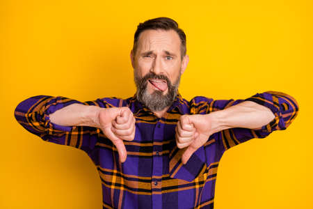 Photo of displease unhappy mature man make thumbs down dislike bad mood isolated on yellow color backgroundの写真素材