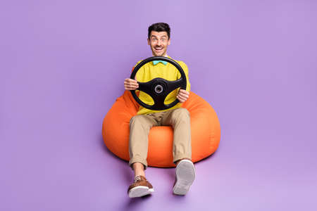 Full size photo of brunet optimistic guy sit on bag with wheel wear yellow sweater trousers sneakers...