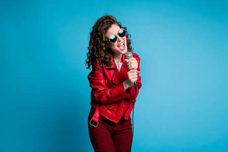 Portrait of pretty wavy hairdo lady two hands hold mic open mouth yell singing isolated on blue color backgroundの写真素材