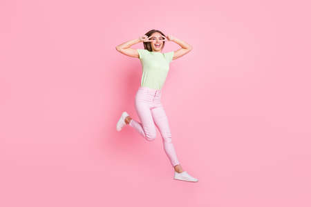 Full size portrait of adorable girl jumping high show two hands fingers v-sign near eyes isolated on...