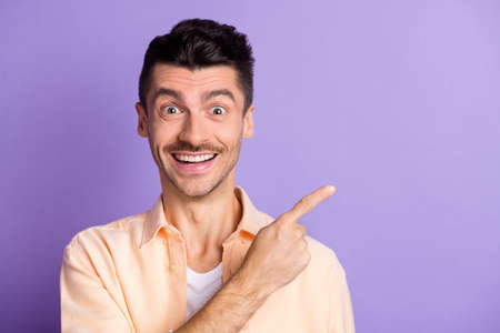 Photo of excited guy direct forefinger empty space wear beige shirt isolated violet color backgroundの写真素材
