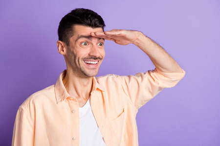 Portrait of funny brunet hair guy look hand head wear peach shirt isolated on lilac color backgroundの写真素材