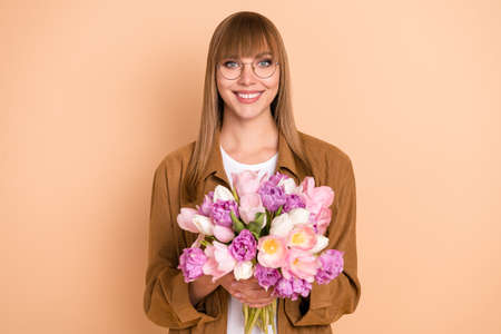 Photo of charming happy nice young woman hold flowers tulip isolated on pastel beige color backgroundの写真素材