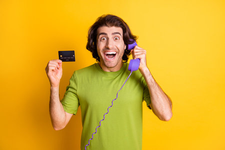 Photo of funny excited man hold telephone talk show debit card wear green t-shirt isolated yellow...