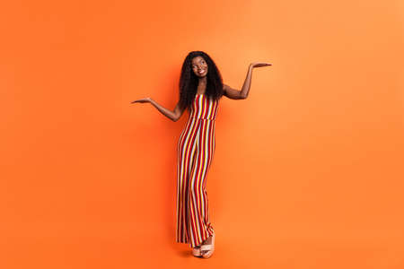 Full body photo of dark skin dreamy lady look empty space hold hands scales isolated on orange color backgroundの写真素材
