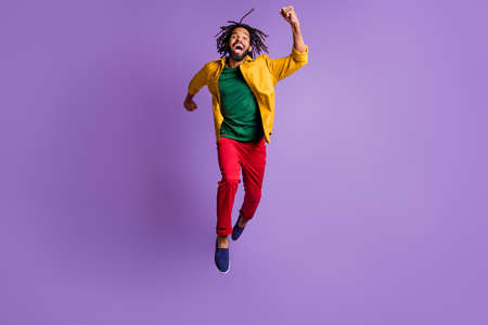 Full length photo of excited dark skin guy dressed yellow shirt jumping high running fast isolated purple color backgroundの写真素材