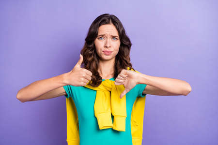 Portrait of lovely puzzled wavy-haired girl showing thumbup and down choose reaction isolated over...