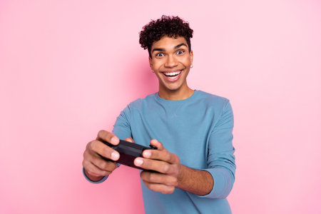 Photo of young cheerful afro man happy positive smile hold joystick play game isolated over pink...