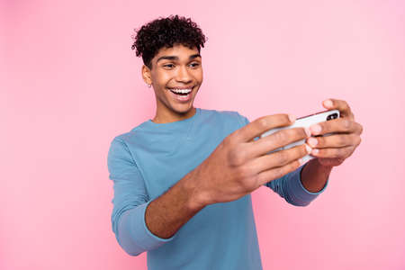 Photo of young excited black guy happy positive smile play game smartphone isolated over pastel...