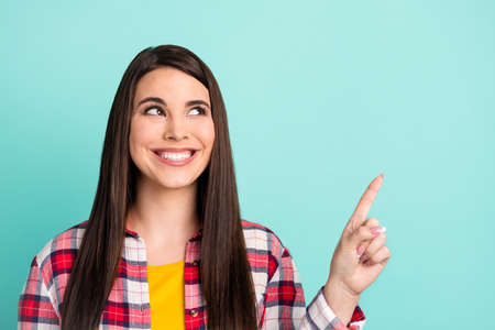 Photo of positive attractive young woman point look empty space recommend promo isolated on teal color backgroundの写真素材