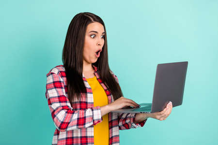 Photo of amazed shocked young woman hold look laptop unexpected news isolated on teal color backgroundの写真素材